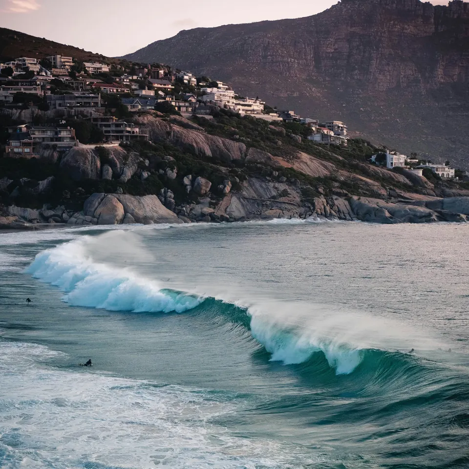 A wave breaking below boulders and hillside houses on Cape Town’s Atlantic coast.