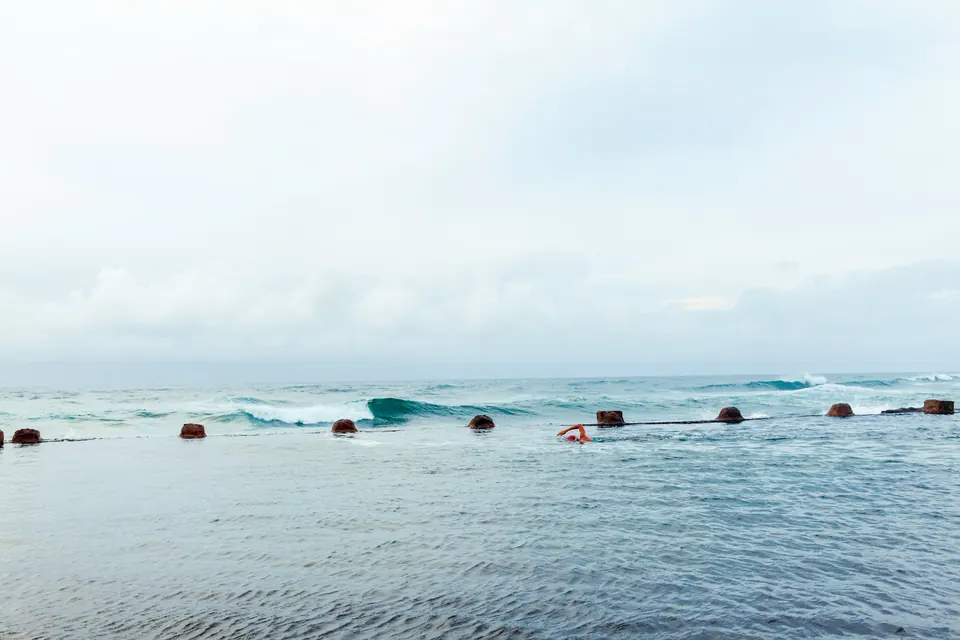 A swimmer in an ocean tidal pool in Durban, with waves breaking beyond the pool wall.