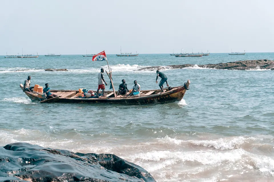 A wooden fishing boat with its crew in the surf at Elmina, Ghana.