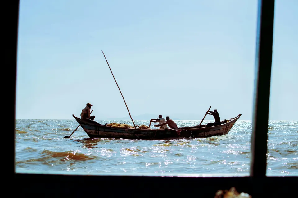 Men rowing a wooden fishing boat on Lake Victoria near Kisumu, framed by a window.