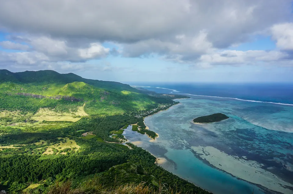 Aerial view of green hills meeting the lagoon and reef at Le Morne, Mauritius.