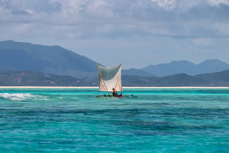 A sailing canoe on turquoise water off Madagascar, with mountains beyond.