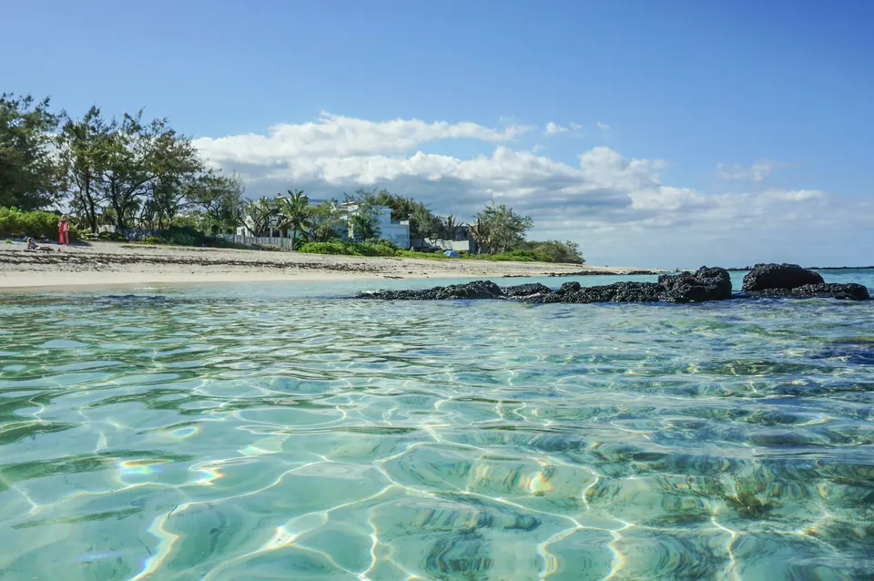 Clear turquoise water over a sandy bottom, with a palm-lined shore beyond, in Mauritius.