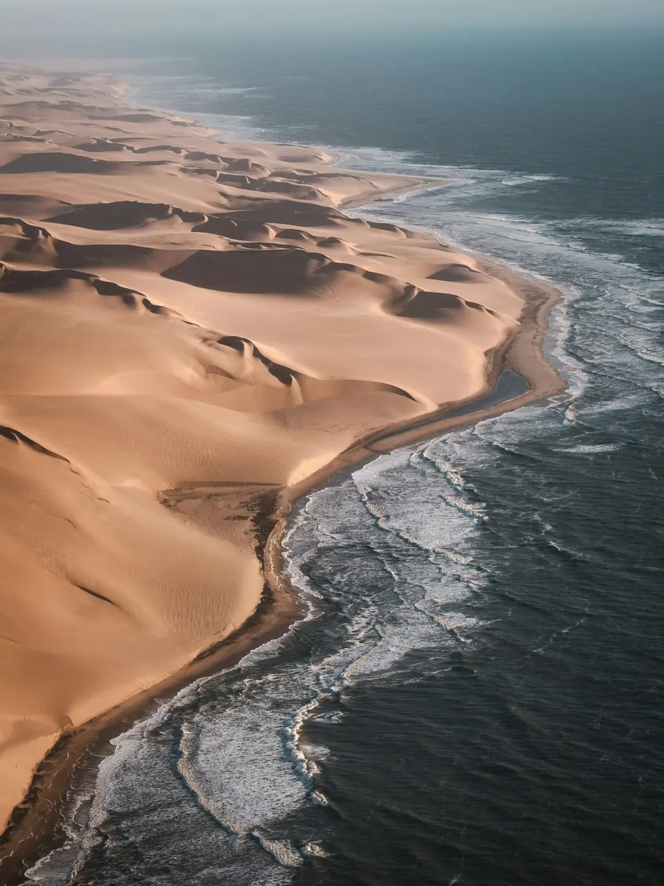 Aerial view of desert dunes meeting Atlantic surf in the Namib-Naukluft National Park, Namibia.