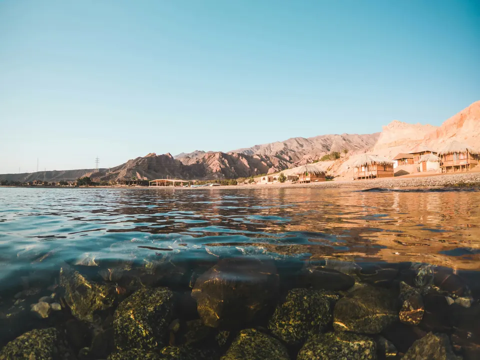 Clear, still Red Sea water over rocks at Nuweiba, with the Sinai mountains beyond.