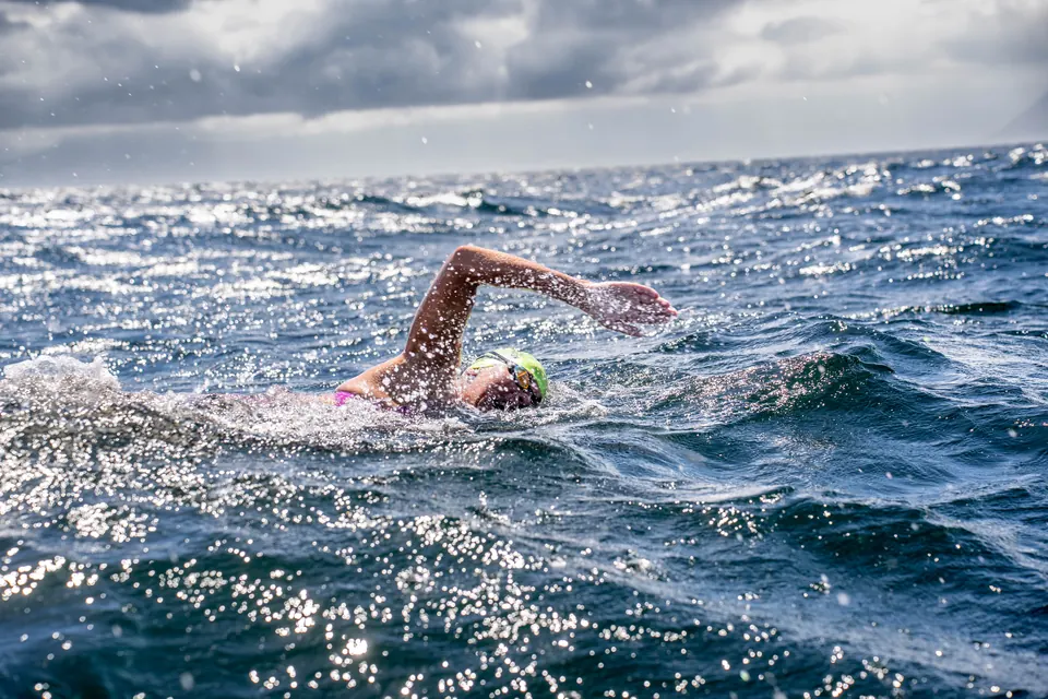 A marathon swimmer doing front crawl through choppy, sunlit open water.